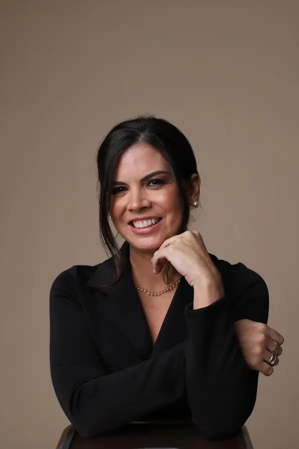 Retrato de Nathalia Moura sorrindo, de blusa preta, com a mão apoiada no queixo
