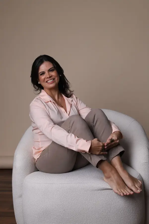 Nathalia Moura sorrindo, sentada em uma poltrona clara com os joelhos dobrados